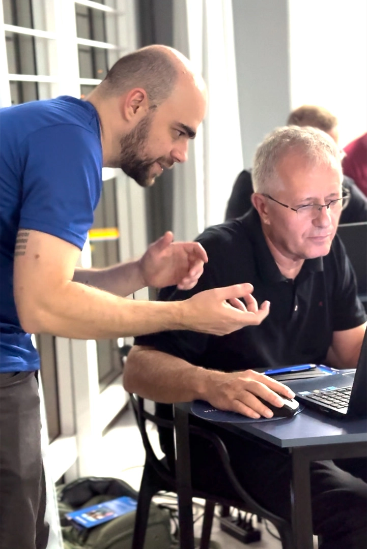 Especialista gesticulando e ensinando aluno adulto enquanto ambos olham para a tela do notebook